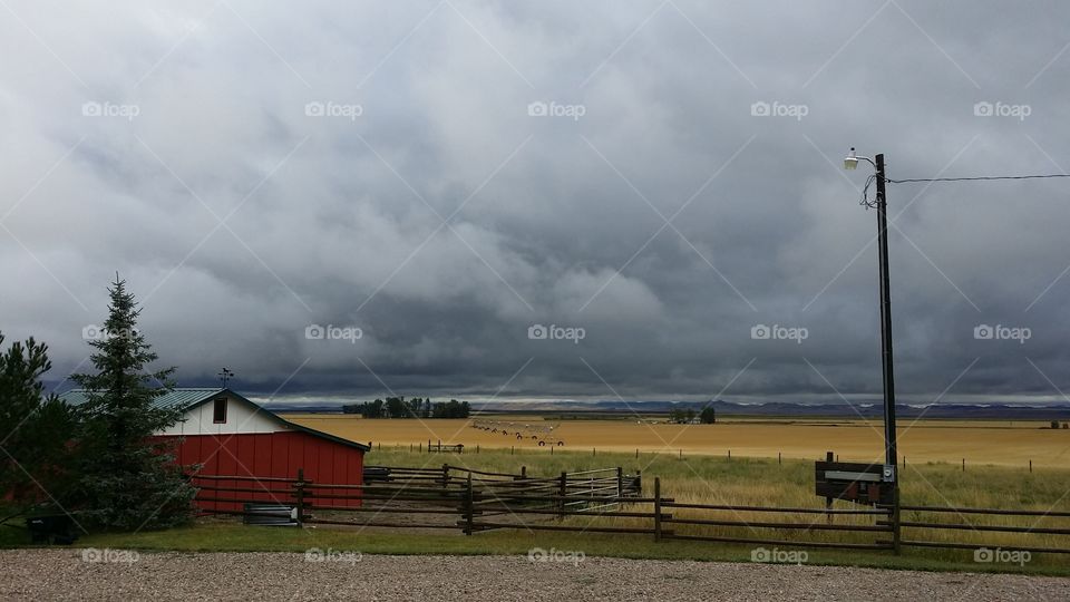 Storm clouds develop behind a red barn on the plains. 