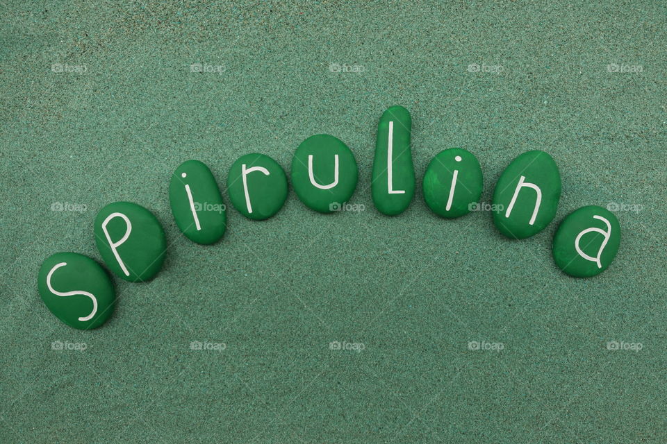 Spirulina word with green painted stones composition over green sand