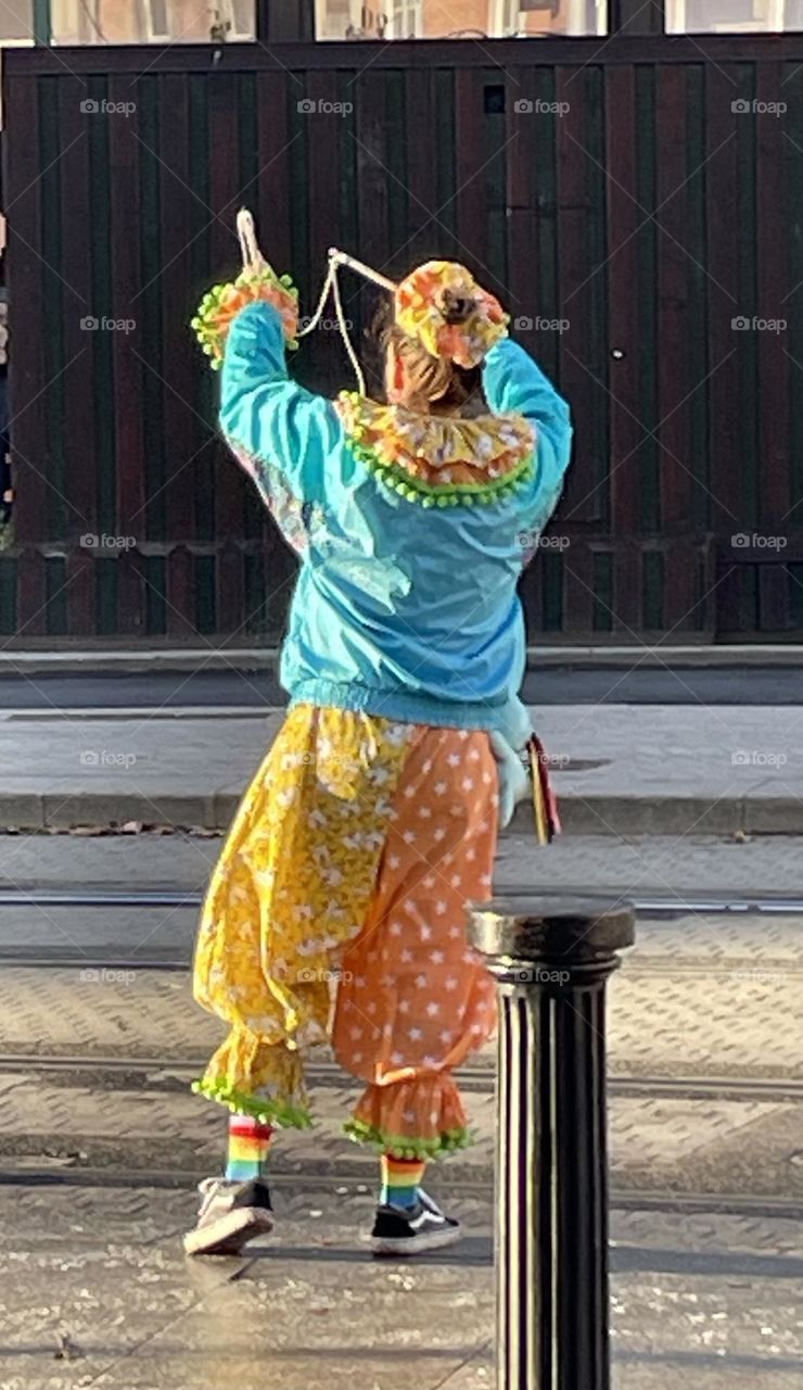 The street performer in Dublin is dressed in a vibrant, eye-catching outfit that stand out against the city's cobbled streets. With his energetic movements and theatrical expressions, he captivates the passing crowd, adding color to the urban scene.