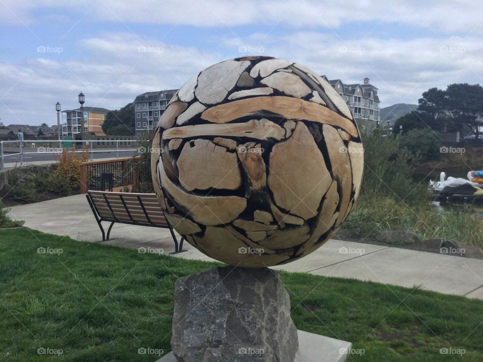 Public Artwork of a Sphere made of wood on a stone base in Seaside, Oregon near the water