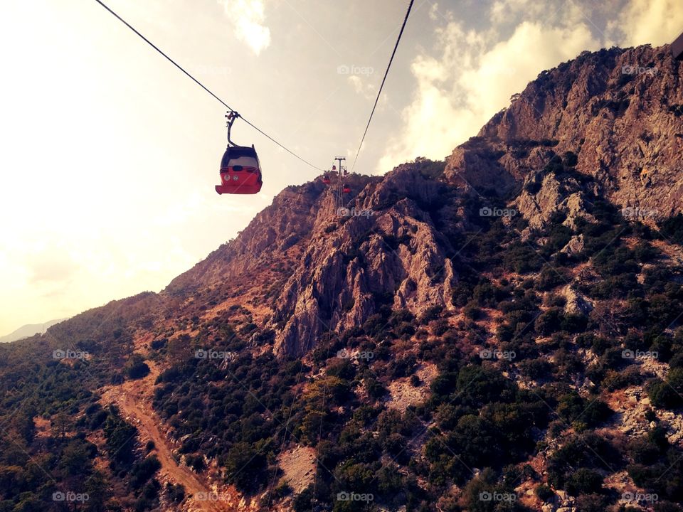 The touristic cable cars on the wire in the mountains with trees and rocks and above the mountain valley. With beautiful sky with white clouds.
