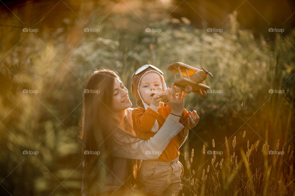 Mother with son playing with wooden plane at sunset