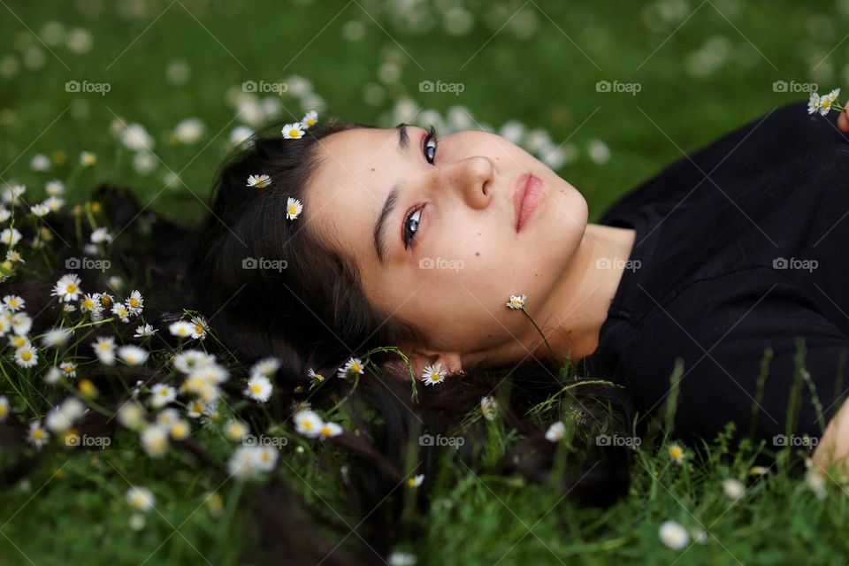 Natural womаn, natural beauty. Beautiful young lady with lovely long hair with daisies lies in the grass. Amazing spring evening in the park.