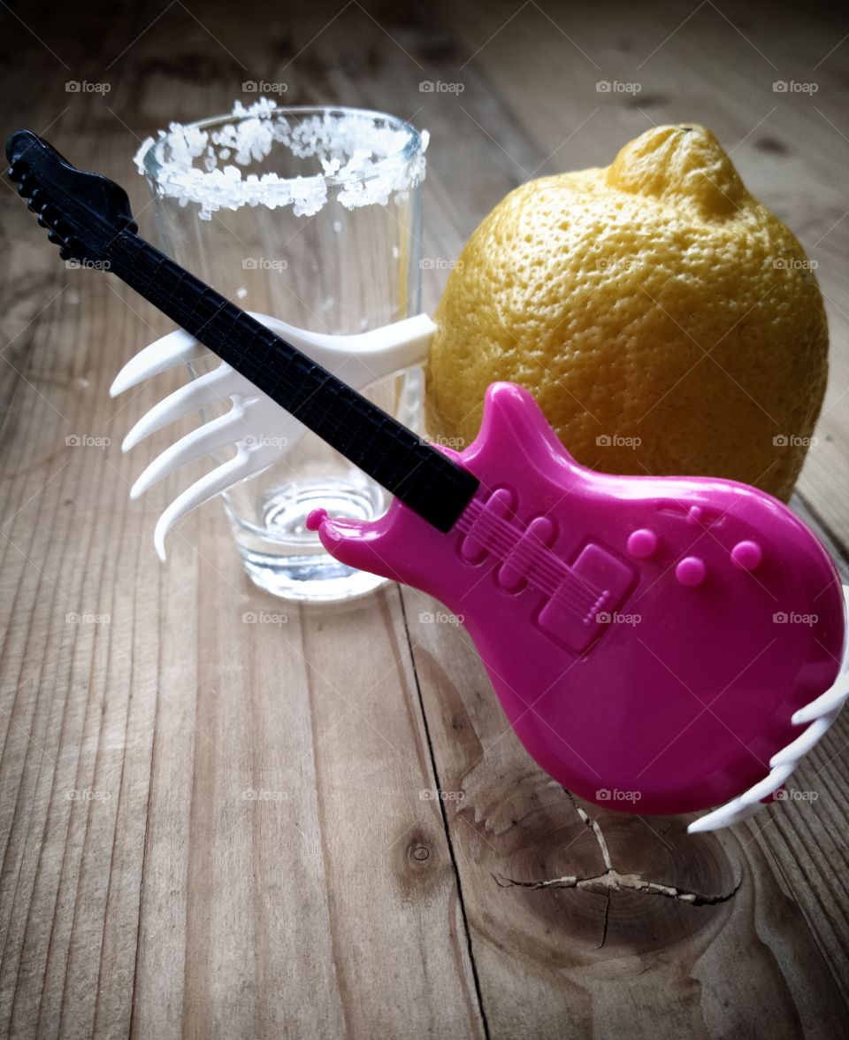 Lemon with hands in the form of two forks, holding a guitar.  Nearby is a glass, the edges of which are decorated with salt.