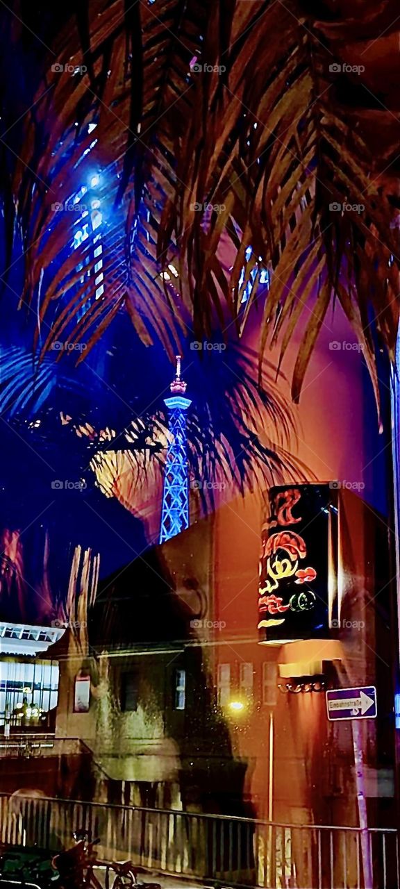 This is a modern hotel in “Berlin” the now again capitol of “Germany”. The lit up structure behind the palm trees is the “Funkturm”, a broadcast tower on “Alexanderplatz” in former “East Berlin”. 2023. Hypnotic Productions