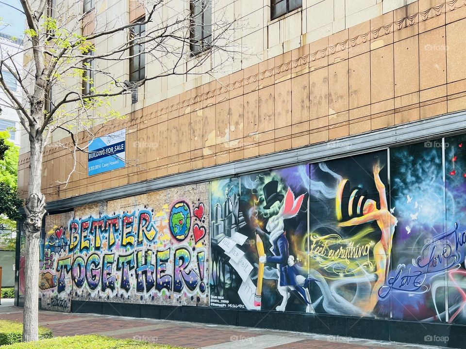 Positive message in graffiti on urban building. The images of the old store are barely visible above the colorful street art.