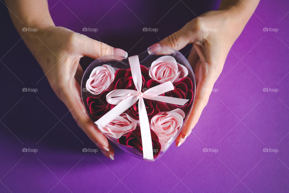 Hands holding a heart shaped box on the purple bacground