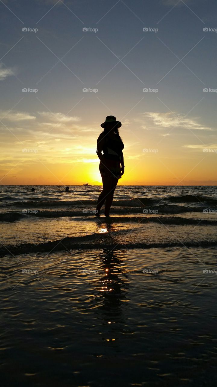 Silhouette of woman standing in sea at sunset