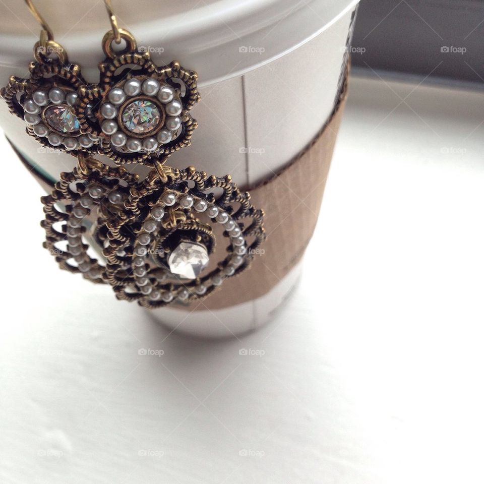 Beautiful pearl and diamond statement Earrings hanging on a to-go coffee cup