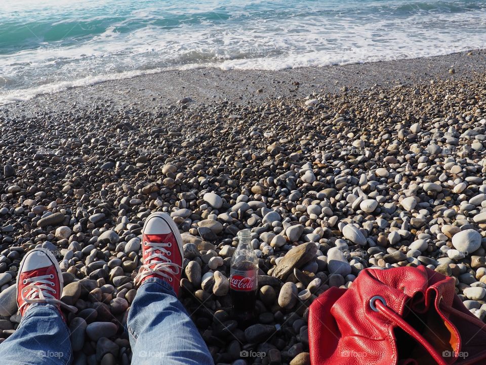 A bottle of Diet Coke on the beach with red sneakers and red leather bag.