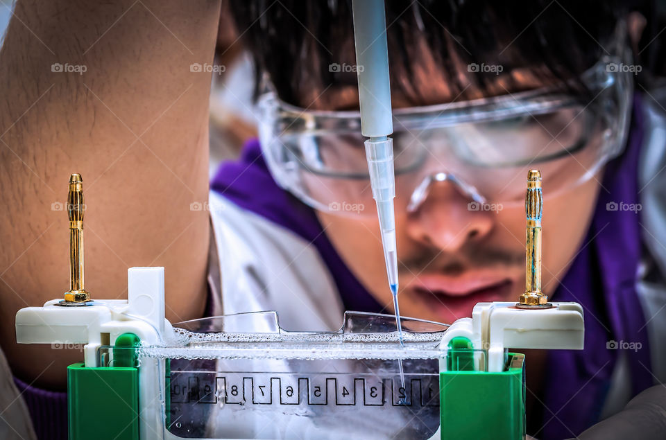 A young scientist demonstrates the delicate process of loading a liquid sample, using an autopipette, into a gel well for electrophoretic separation under the influence of an applied current.