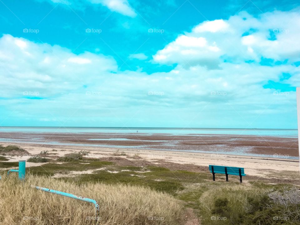 Single blue turquoise Aqua bench on a remote beach at the ocean south Australia low tide 