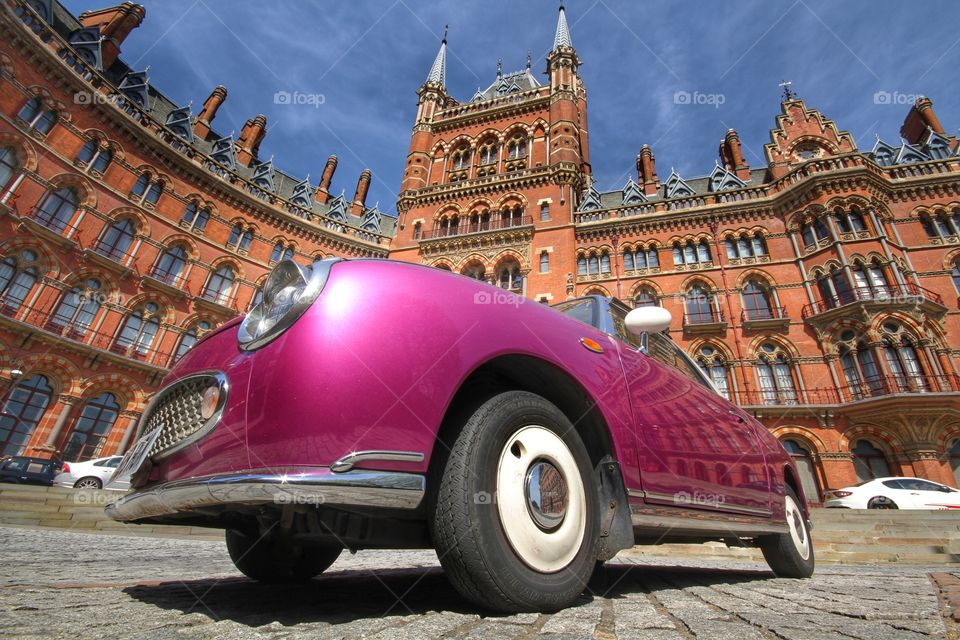 A classic purple car from a low viewpoint with the St Pancras hotel in London behind.