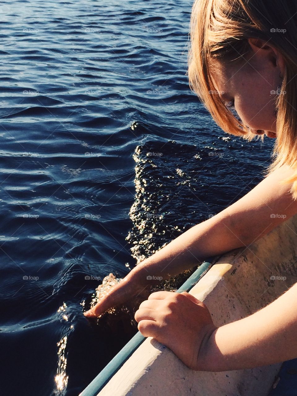 Summer. Girl holding her hand in the water from the boat