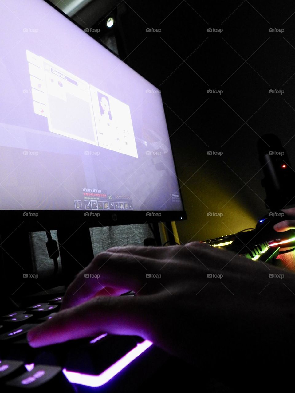 Teenager boy playing Minecraft on the gaming computer seen from his left side and close-up of his hand playing in a dark room.