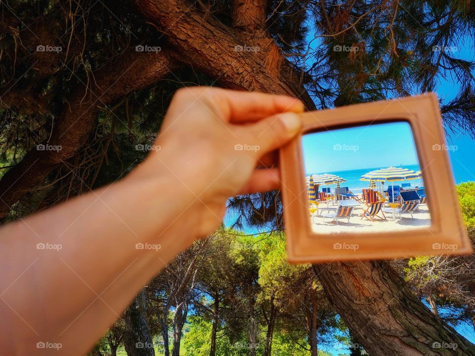 hand holds a mirror that reflects the beach and the umbrellas by the sea