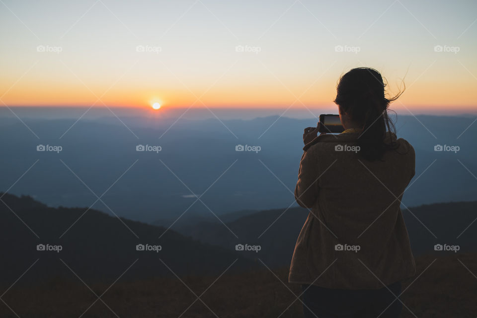 Asian woman travelers taking photos of the sunset with mobile phone