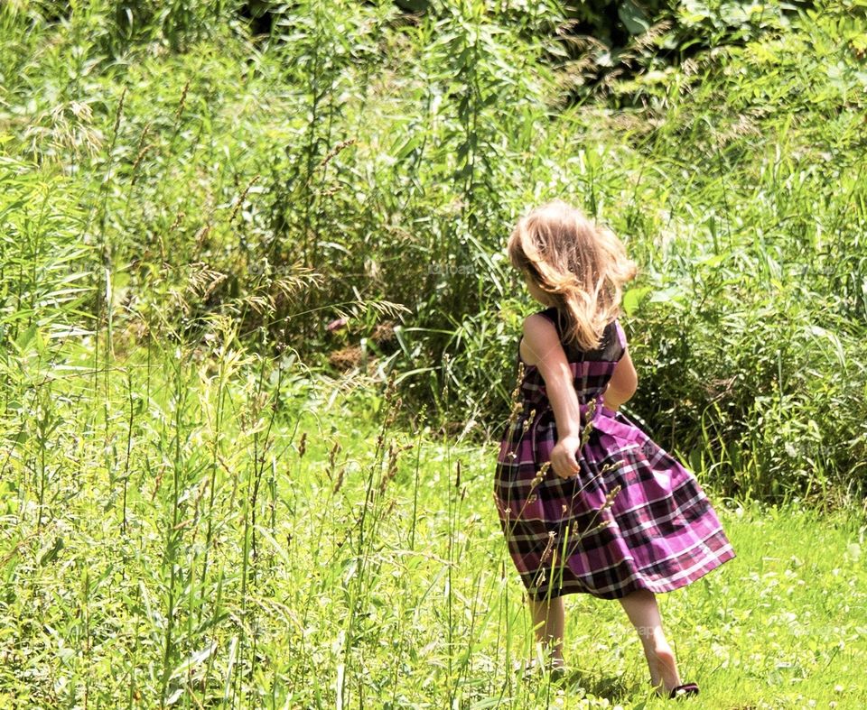 Little girl in a purple dress walking through a field 