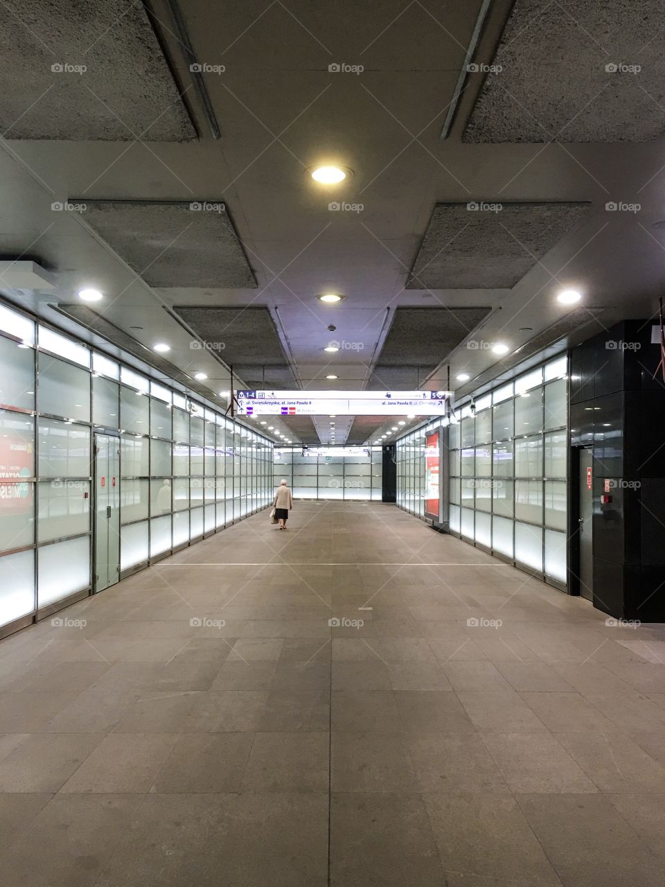A lonely old woman crossing underground passage. View from behind from a distance.