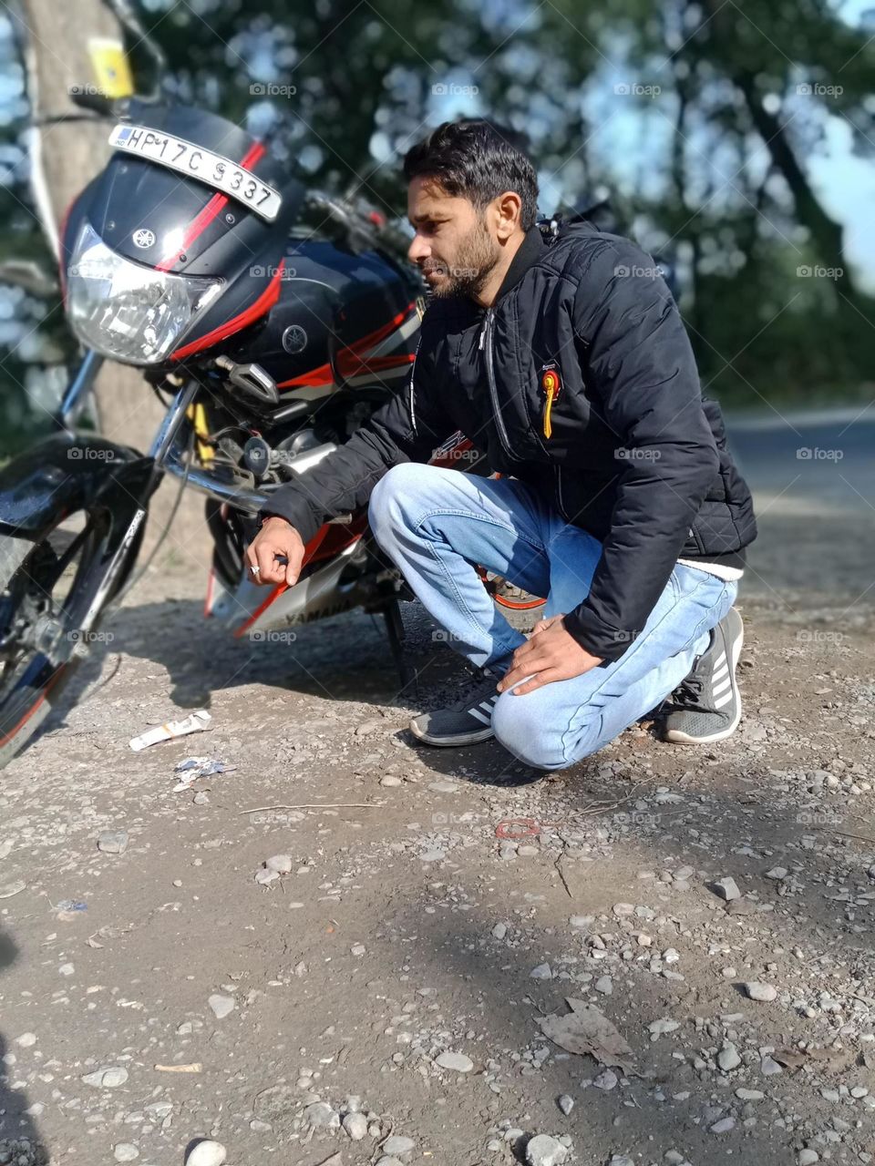 A young man confidently posing with his Yamaha sports bike on a peaceful mountain road in India. Surrounded by nature and trees, the scene captures the thrill of adventure and the spirit of biking. Perfect blend of lifestyle and travel photography