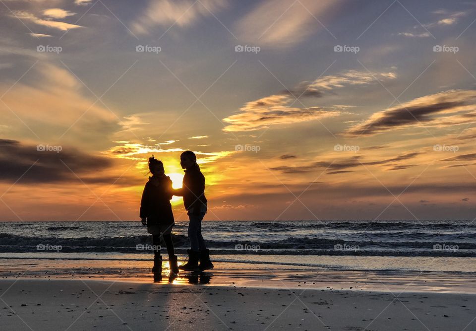 Two girls playing at the beach while the sun sets