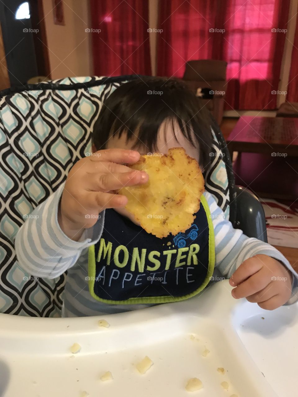 A boy wondered by tostones. A toddler eating happily. 