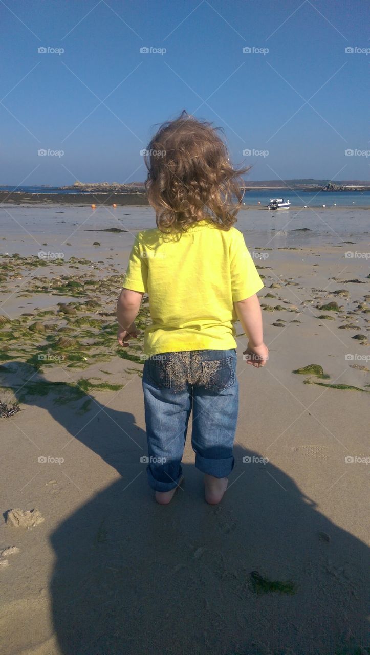 back of small child standing on beach looking put to see with Sandy bottom.