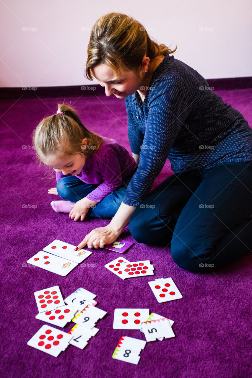 Mother teaching counting her little daughter using card game sitting on a carpet at home