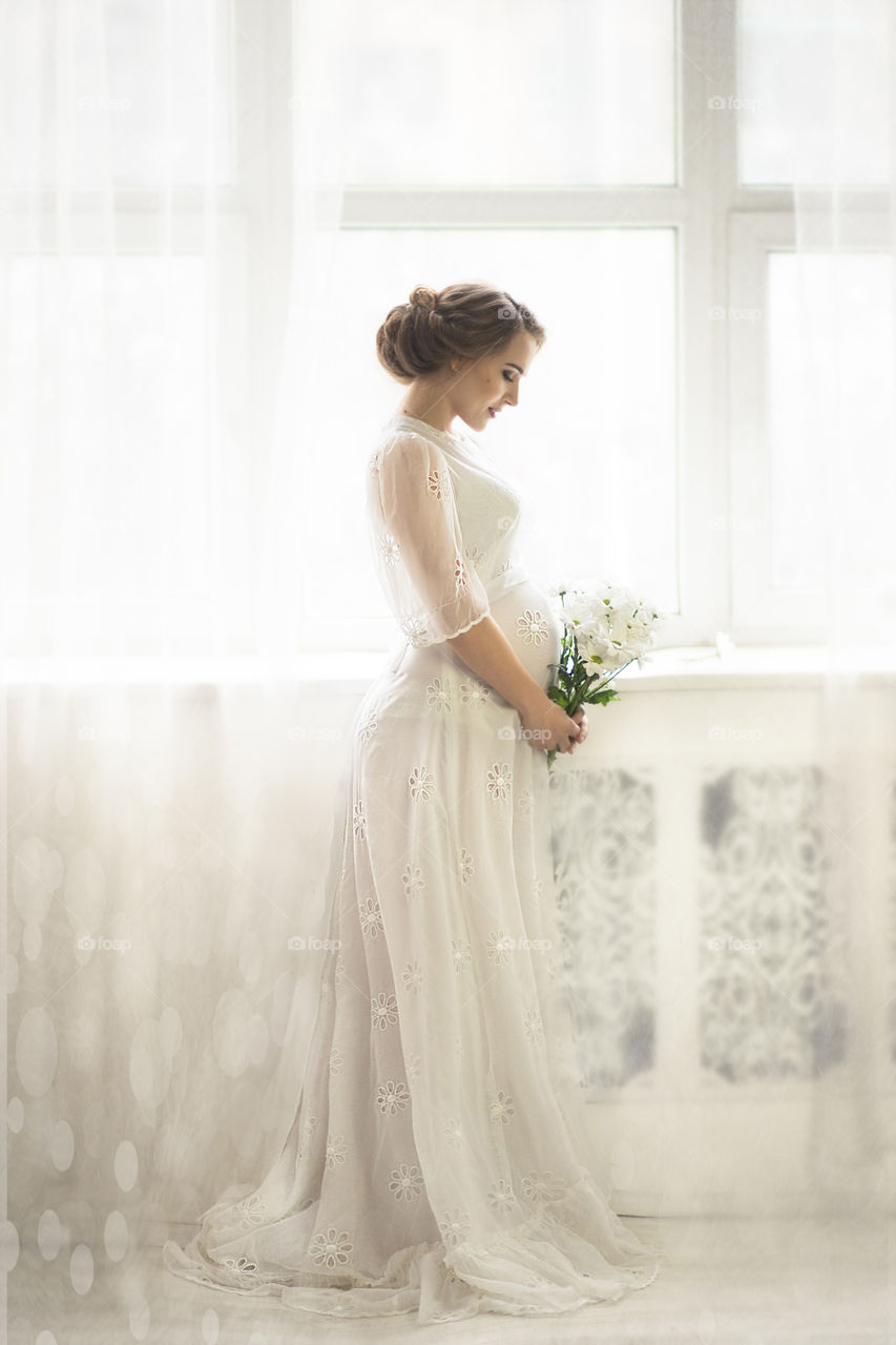 pregnant woman in a white dress by the window