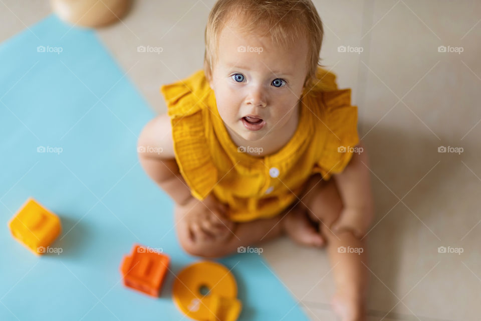 Cute Caucasian baby girl in orange dress sitting on blue background 
