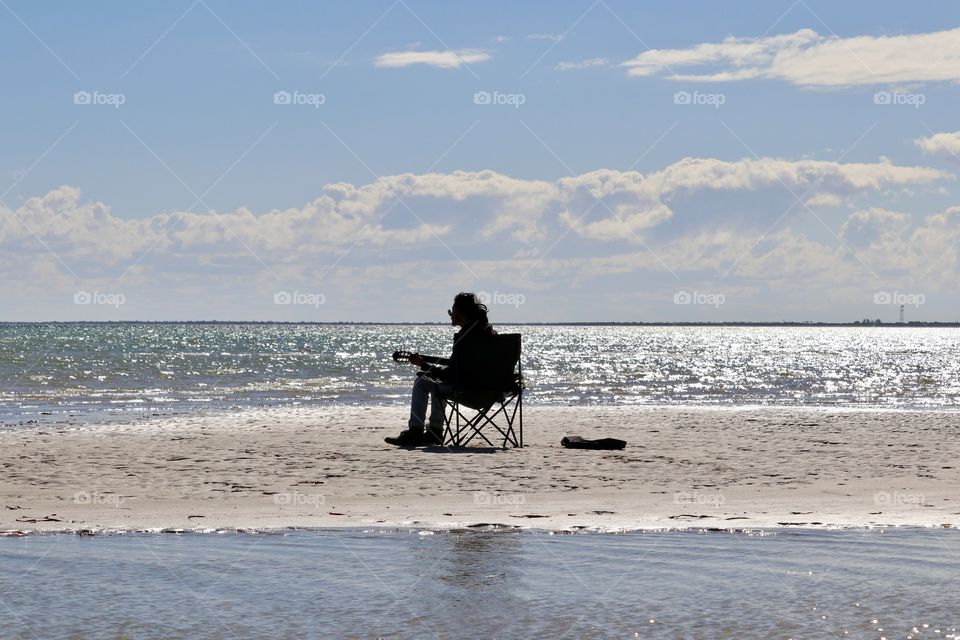 Musician with guitar alone on the surrounded by ocean 