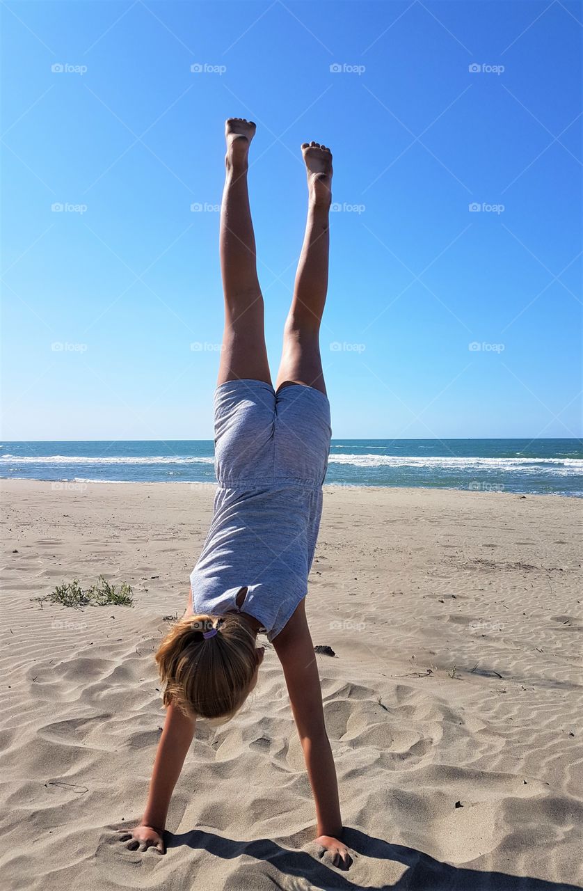 a girl is doing a handstand on the beach