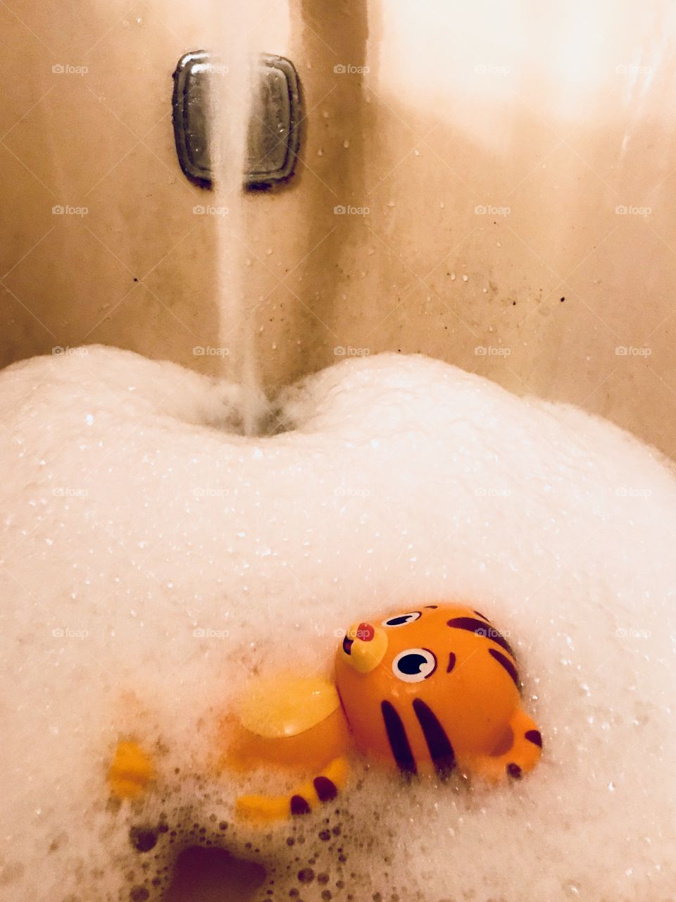 Daniel tiger toy floating in the bathtub filled with bubbles while the water is flowing from the faucet filling the tub