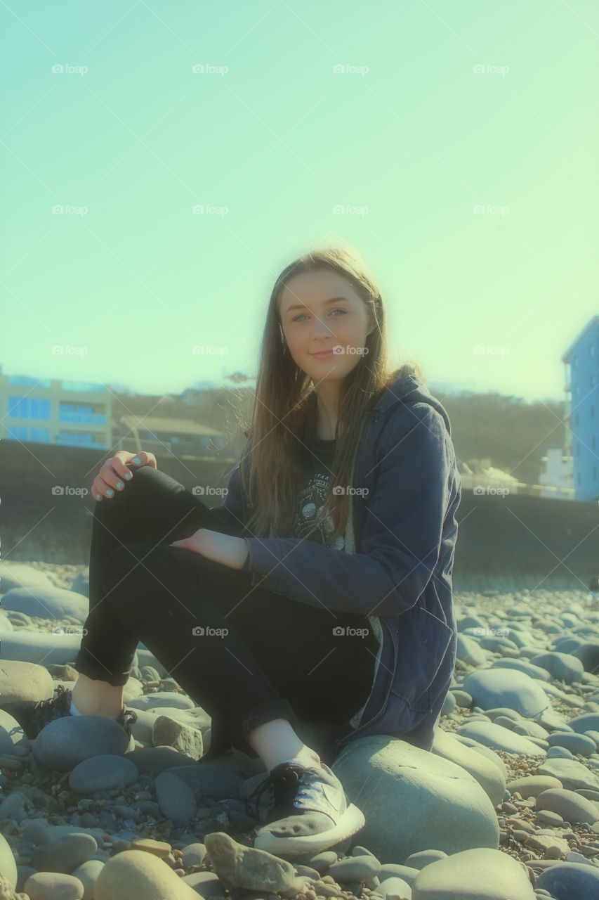 Teenage smiling girl sitting on pebble