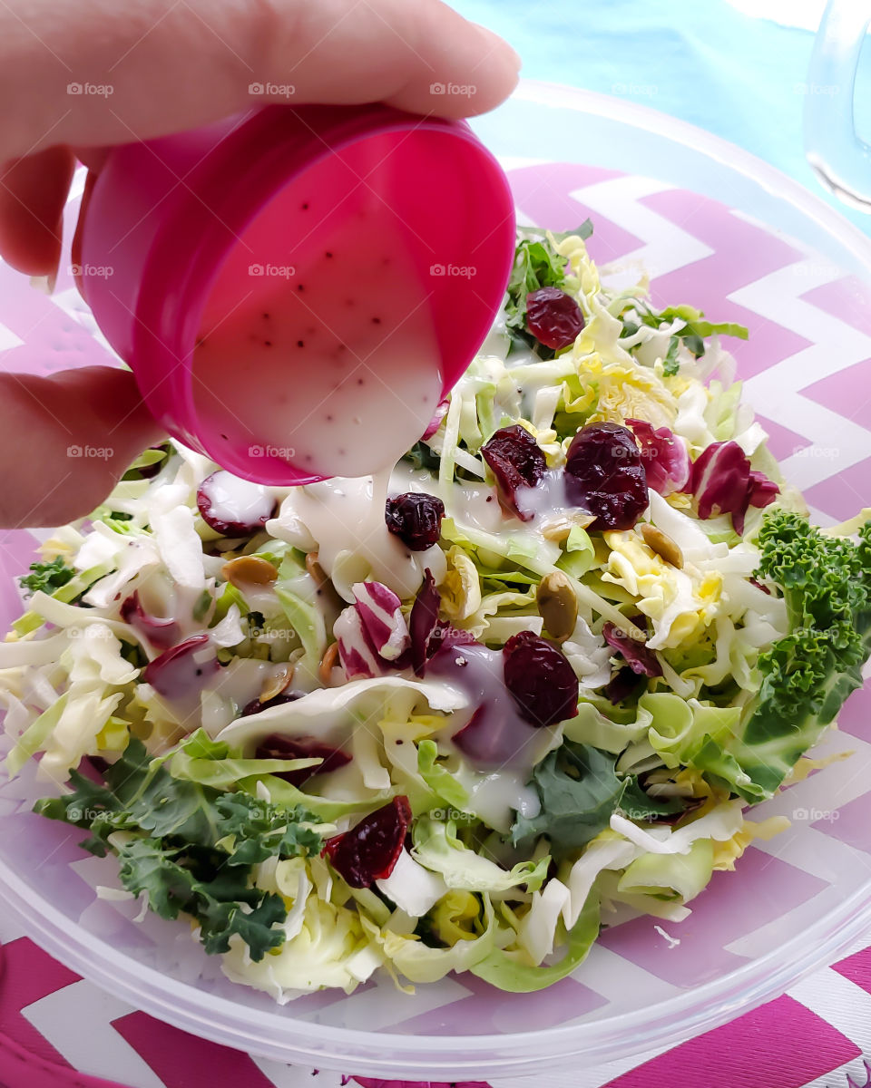 Healthy sweet and crunchy kale salad snack with cranberries and pumpkin seeds with dressing being poured on it.