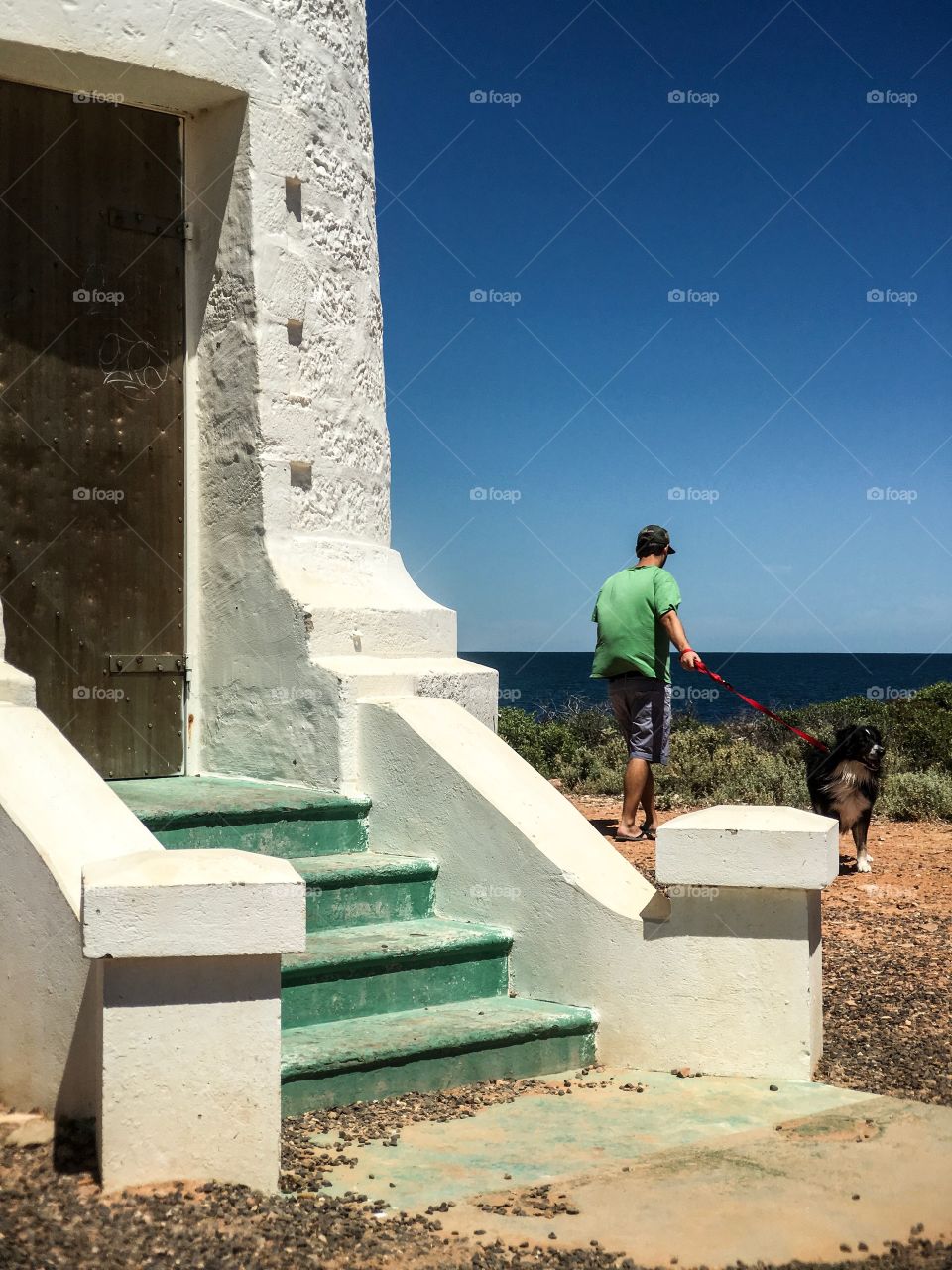 Young man walking his border collie sheepdog by lighthouse on bright blue sunny day Oceanside 