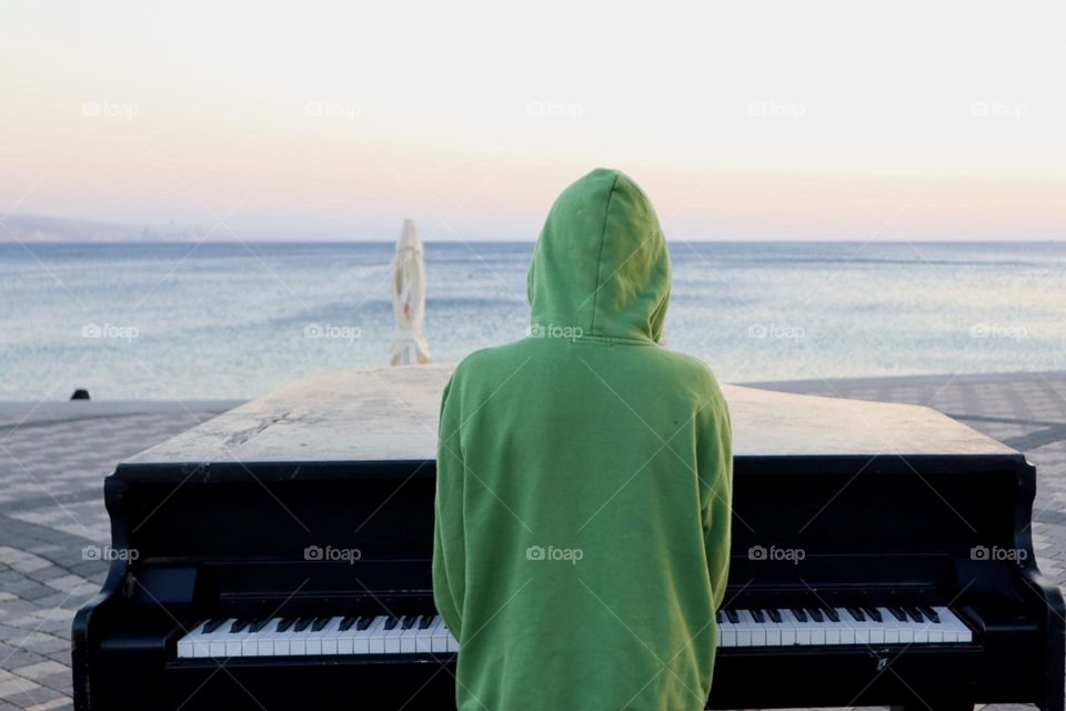 Kid play piano viewing calm sea with sunset light