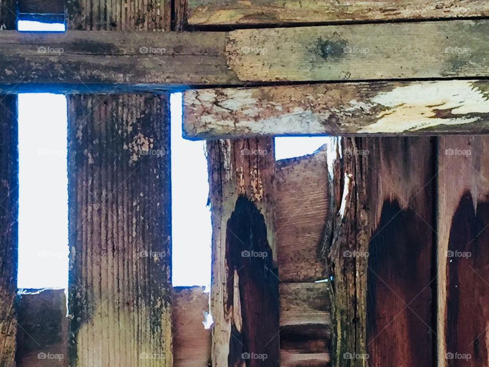 A view of a bright  sky seen through the wooden rafters of an old structure