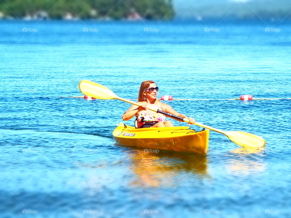 Woman in yellow kayak paddling in lake winnipesaukee in summer - selective focus 