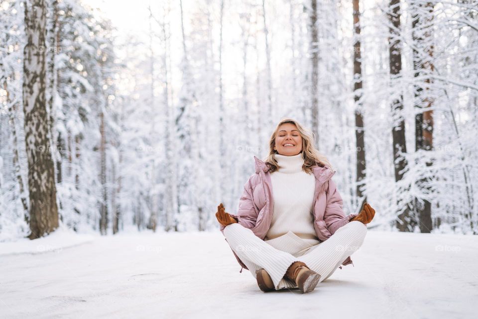 Portrait of smiling blonde woman with blonde hair in winter clothes in snowy winter forest