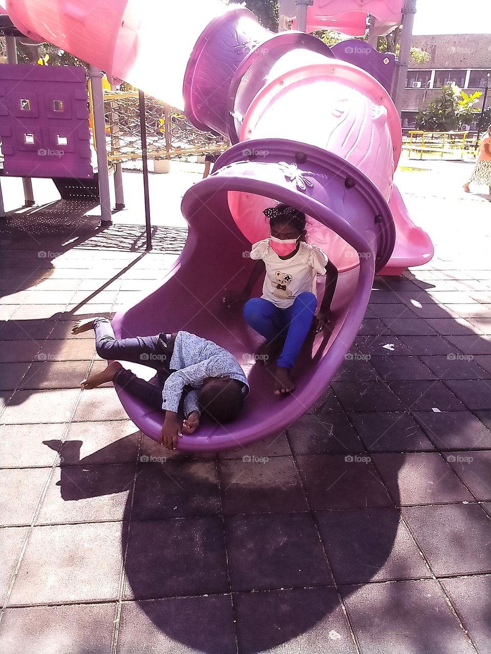 This is a capture of a children's park. There is a tunnel and two children are playing with tunnel . the shadows are so clear and they seems like enjoining and play funny.