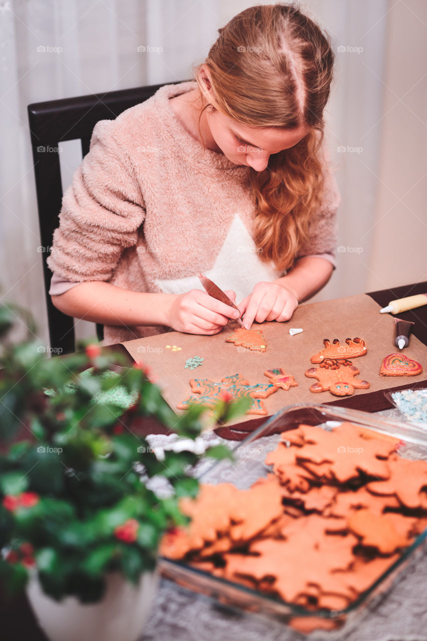 Girl decorating baked Christmas gingerbread cookies with chocolate writing pen