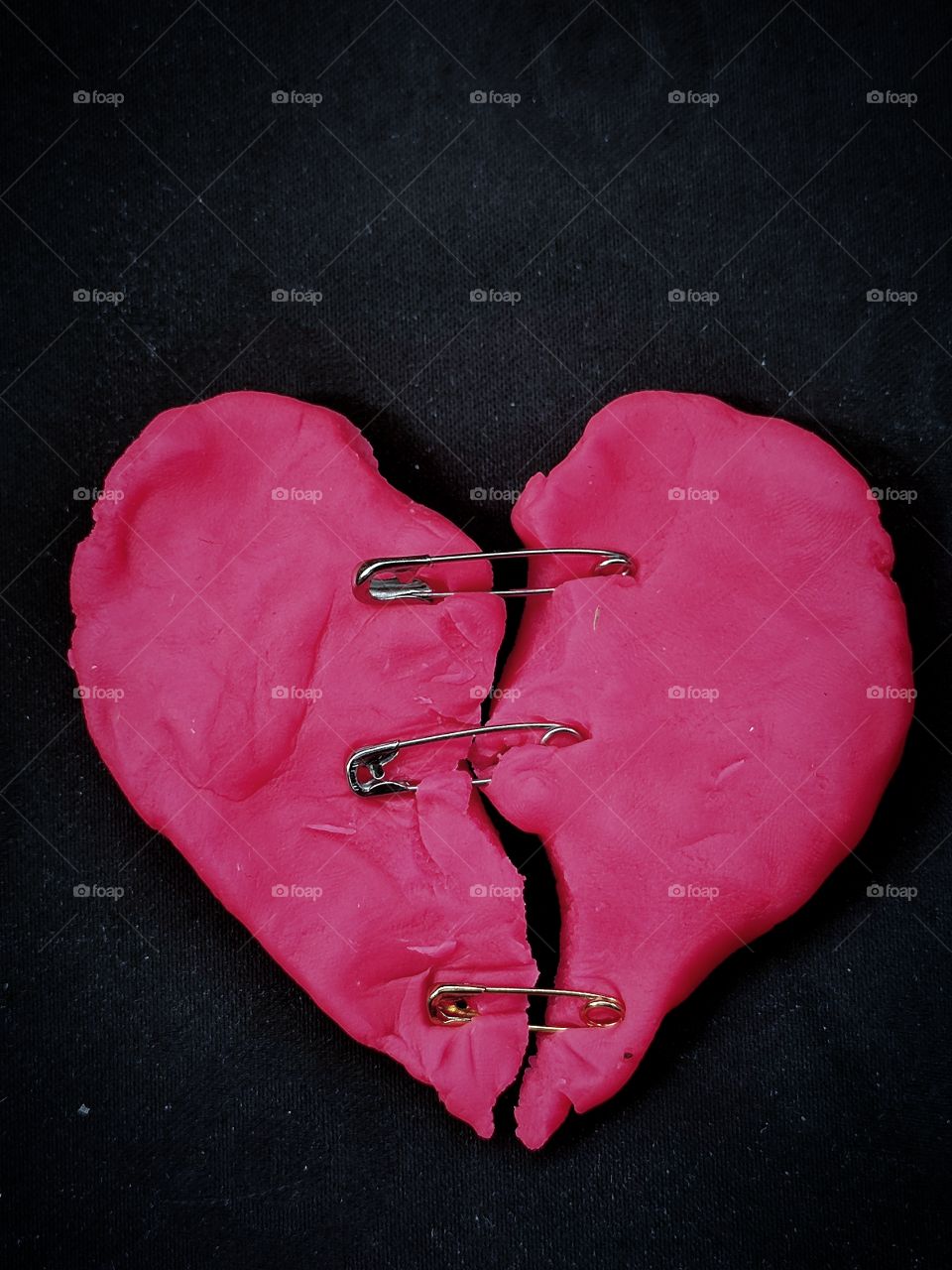 pink "torn" heart fastened with metal pins on a black background