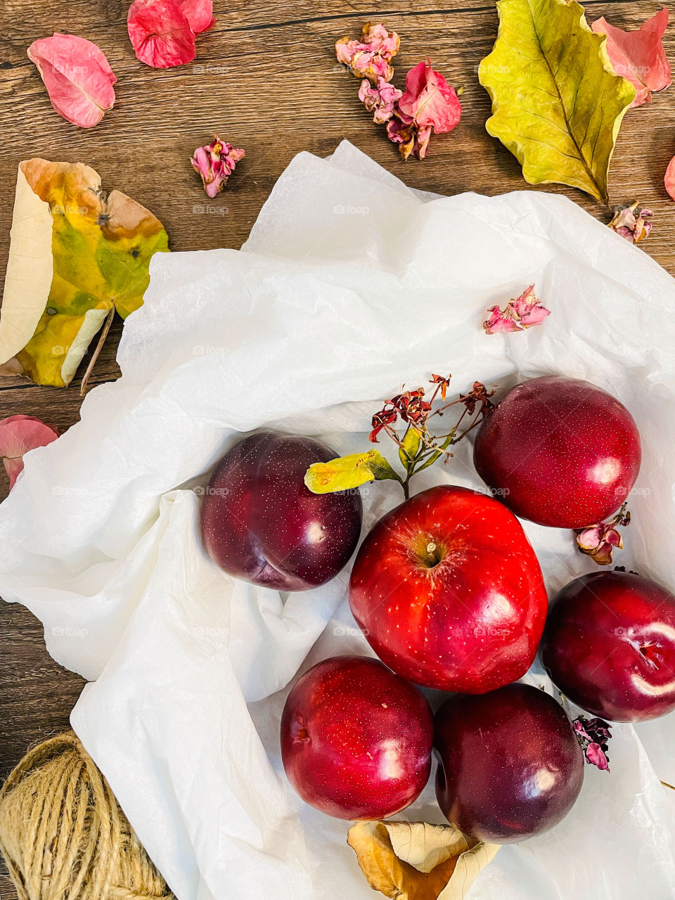 Plums and apple on a white paper and wooden background with dried flowers and leaves .Flat lays 