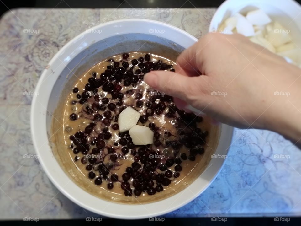 Woman's hand putting pears on top of an old-fashioned blueberry pear cobbler before being baked