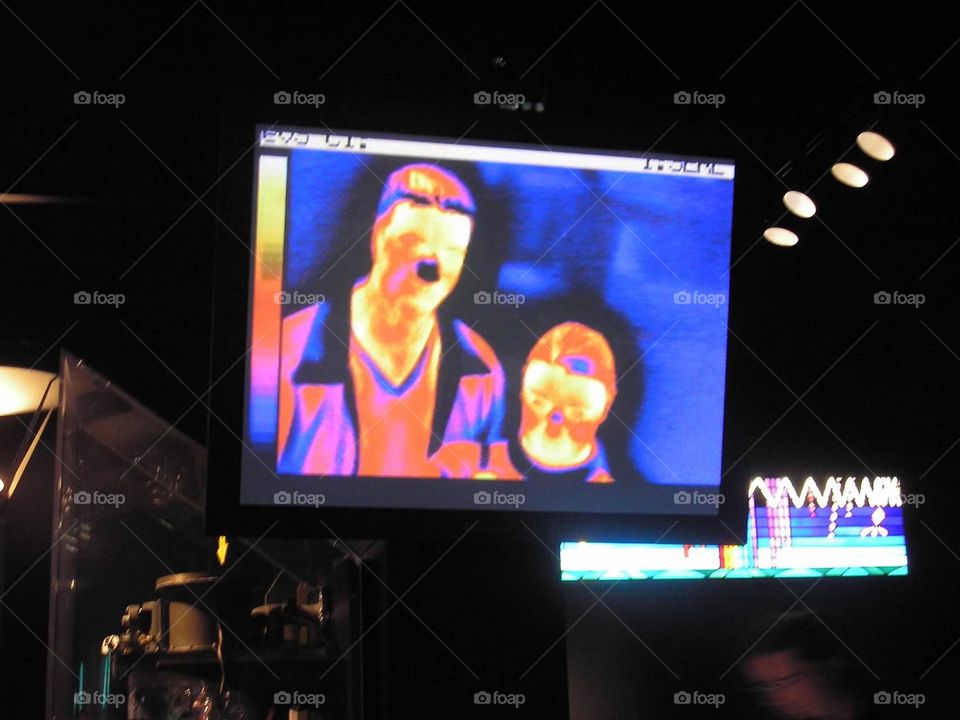 A couple stand in front of a heat-sensing camera showing the differences in body temperatures on a display screen. Thermal topography. 