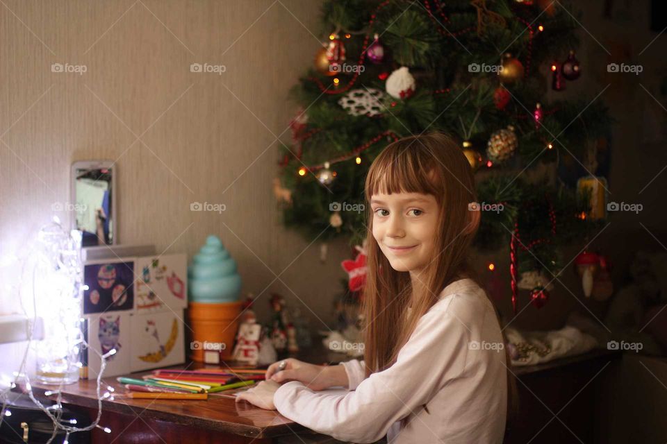 Little girl draws with pencils on the table under the Christmas tree