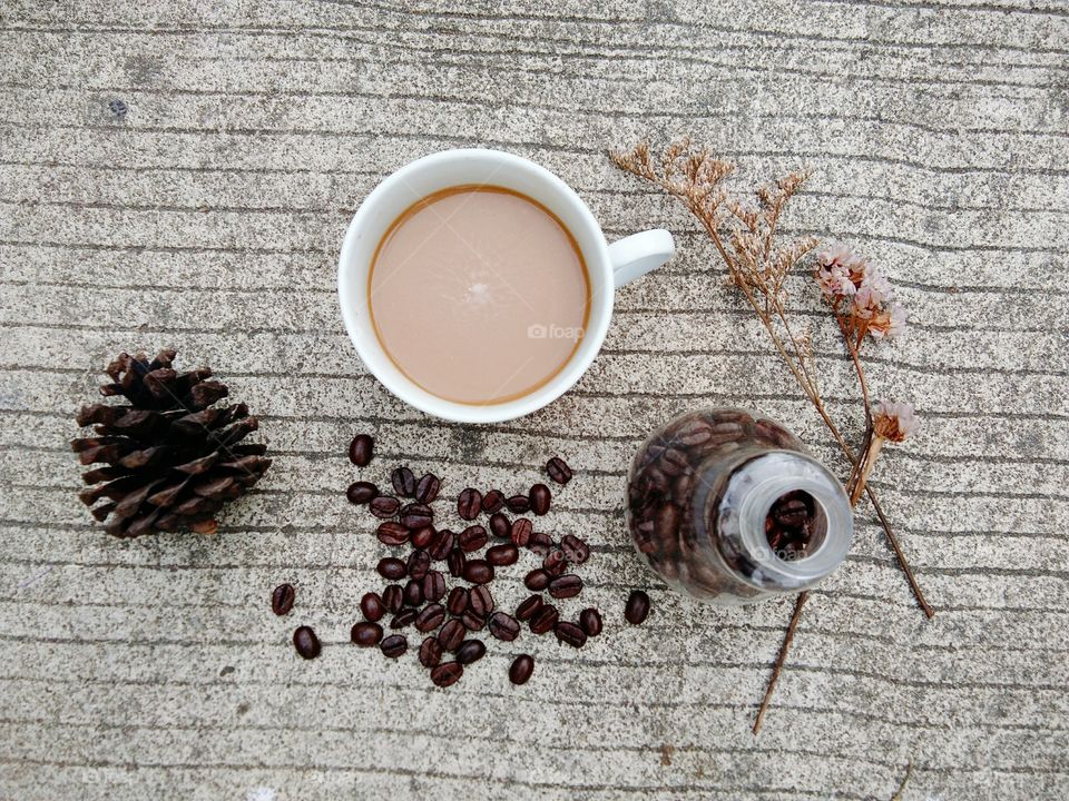 A White cup of coffee and coffee beans in glass bottle on concrete floor