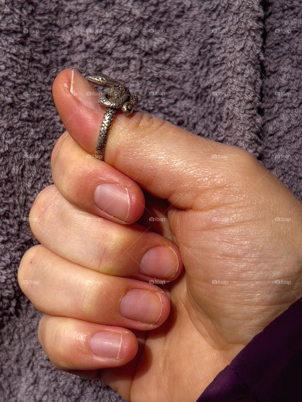 Hand wearing snake-shaped ring on the thumb while the snake is facing towards the finger.