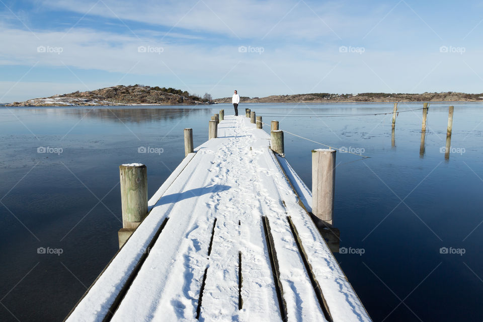 Man standing on a wooden jetty covered in snow in frozen ocean, beautiful cold winter day 